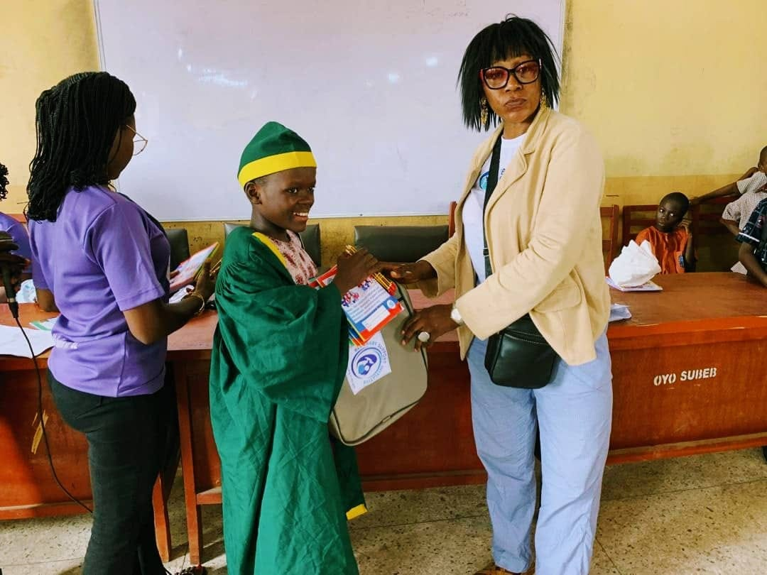 A BBSI volunteer handing a school backpack to a graduating pupil